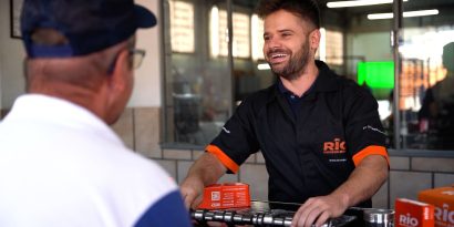 Balconista de autopeças atende mecânico no balcão com componentes de motor, representando a venda técnica de peças para motor no mercado de reposição