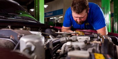 Mecânico avalia o motor de um veículo para evitar retrabalho na oficina mecânica.